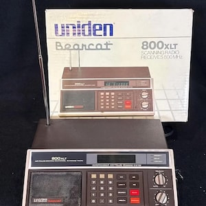 Może przedstawiać: Zabytkowe radio skanujące Uniden Bearcat 800XLT w kolorze brązowo-białym. Radio posiada klawiaturę, wyświetlacz i antenę. Pudełko z tyłu radia również wyświetla model i markę radia.