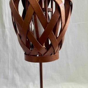 May include: A decorative copper-colored candle holder with a woven basket design. The holder features a clear glass insert and sits on a clear, faceted glass base. The candle holder is a unique home decor item.