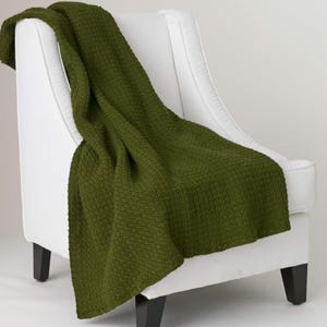 Könnte beinhalten: Eine olivgrüne Decke mit strukturierter Webung, die über einem weißen Sessel drapiert ist. Die Decke bietet einen Farbtupfer vor dem weißen Stuhl. Der Stuhl hat schwarze Beine. Die Decke ist ca. 150 cm x 200 cm groß.