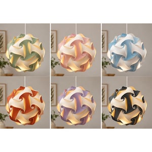 Peut inclure: Une collection de six lampes suspendues sphériques, chacune présentant un design modulaire imbriqué. Les lampes sont présentées en différentes couleurs, notamment vert sauge, rose pâle, bleu clair, orange brûlé, lavande et noir, associées au blanc.