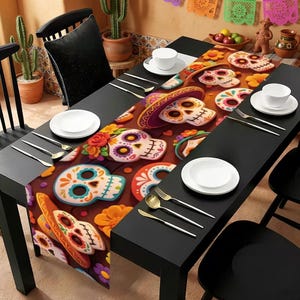 Puede incluir: Un camino de mesa con un patrón repetitivo de calaveras de azúcar coloridas, flores de cempasúchil y sombreros sobre un fondo marrón oscuro, colocado en una mesa de comedor negra con platos blancos, tenedores y cuchillos de plata.