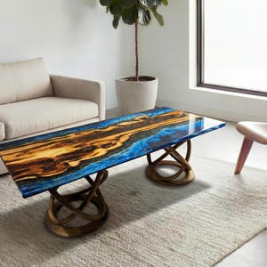 Puede incluir: Una mesa de centro rectangular con un diseño único. La tapa presenta una mezcla de tonos azules, marrones y dorados, que recuerdan a un paisaje natural. La base está hecha de elementos de madera entrelazados. La mesa es un punto focal en un salón moderno.