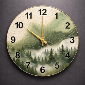 May include: A round wall clock with a gold frame and black numerals. The clock face features a printed design of a misty pine forest at the bottom, transitioning into abstract green and cream topographic contour lines toward the top center.