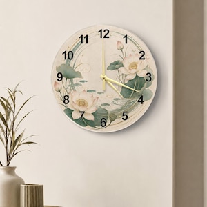 Peut inclure: Une horloge murale ronde avec un cadran couleur crème et des chiffres noirs de 1 à 12. Le motif présente des fleurs de lotus rose pâle, des nénuphars verts et des lignes circulaires dorées. Elle possède trois fines aiguilles dorées.