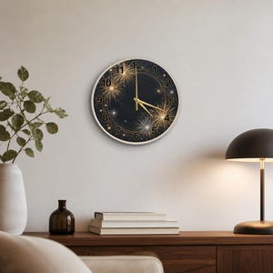 May include: A round wall clock with a black face featuring gold fireworks and starburst designs. The clock has gold hands and a silver-colored frame. Numbers are in gold. The clock is hanging on a white wall.