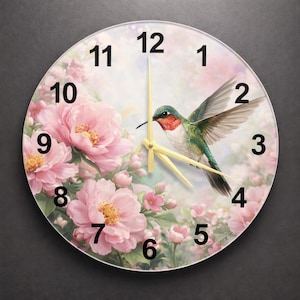 Puede incluir: Reloj de pared redondo con un colibrí y flores rosas. La esfera del reloj tiene números negros y manecillas doradas. El fondo tiene una suave combinación de colores pastel. Ideal para dormitorios o salones.