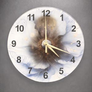 May include: Round wall clock with a floral design. The clock face features a white background with a large, abstract flower in shades of brown, blue, and gold. Black numerals mark the hours, and the clock hands are gold.