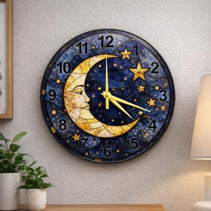 Può includere: Orologio da parete rotondo con un design celeste. Il quadrante presenta una luna crescente con un volto, circondata da stelle su uno sfondo blu scuro. Le lancette dell'orologio sono gialle e i numeri sono in un carattere classico.