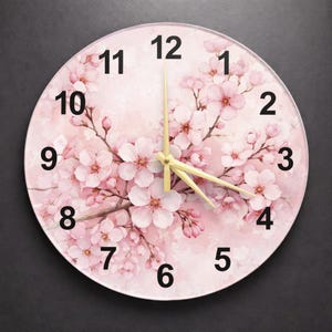 Könnte beinhalten: Runde Wanduhr mit floralem Design aus rosa Kirschblüten. Das Zifferblatt hat schwarze Ziffern und goldfarbene Zeiger. Der Hintergrund ist ein weicher rosa Aquarelleffekt.