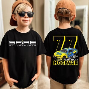 May include: Black t-shirt featuring the "SPIRE MOTORSPORTS" logo in white on the front. The back of the shirt displays the number "77" in yellow, a blue and yellow race car graphic, and the name "CARSON HOGEVAR".