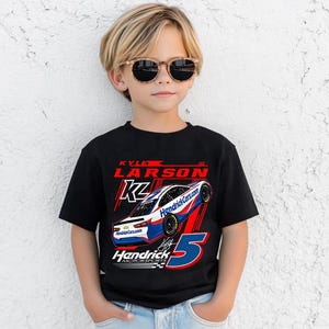 May include: Black t-shirt featuring a race car graphic with the text "KYLE LARSON" and "Hendrick Motorsports". The graphic includes the number 5 in blue and red. The shirt is worn by a child wearing sunglasses.