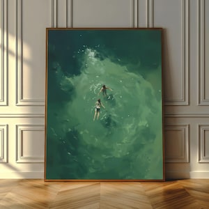 May include: A framed art print depicts two figures swimming in green water. The artwork has a painterly style, with visible brushstrokes creating a sense of movement and depth. The frame is a warm brown color, and the artwork is displayed against a white wall.
