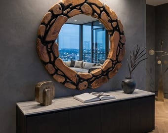 Op de afbeelding: Een grote, ronde spiegel met een uniek houten frame dat is samengesteld uit onregelmatig gevormde stukken. De spiegel hangt boven een zwarte kast met een lichtgekleurd aanrechtblad. Een vaas en decoratieve objecten staan op de kast.