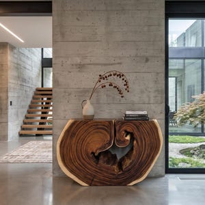 May include: A live edge wood console table with a natural grain pattern and a central hollow void. A two-toned ceramic vase with dried branches sits on the left side, and a stack of two black and white books rests on the right side.