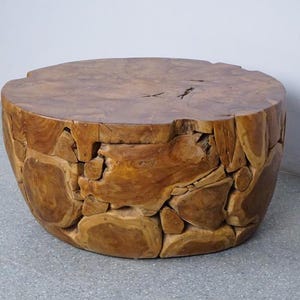 Op de afbeelding: Een ronde, handgemaakte houten salontafel. De tafel is gemaakt van natuurlijk hout, met een lichtbruin blad en een basis die is opgebouwd uit onregelmatig gevormde stukken hout. De tafel heeft een diameter van ongeveer 61 cm en is 46 cm hoog.