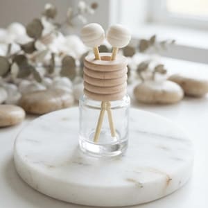 May include: A clear glass bottle topped with a stack of five light-colored wooden rings. Two thin wooden sticks with smooth, round, white spherical ends are inserted through the center of the wooden rings and rest inside the glass bottle.