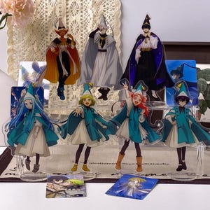May include: A collection of anime-style acrylic character standees featuring various figures in wizard-inspired attire, including pointed hats and capes, displayed on tiered clear stands with additional small rectangular character cards.