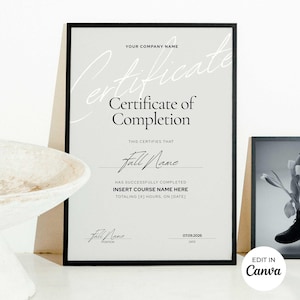 May include: A framed certificate of completion with a black border. The certificate has a light gray background with the words "Certificate of Completion" in a stylish font. The text includes fields for a name, course, hours, and date. The words "Edit in Canva" are in the bottom right corner.