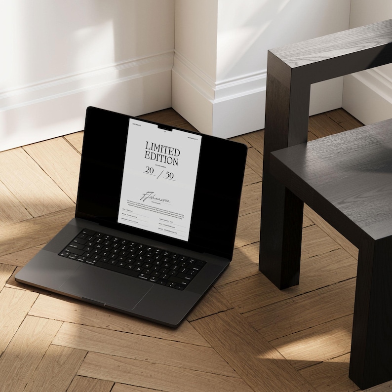 Pode incluir: Um laptop cinza escuro exibindo um documento branco com o texto "LIMITED EDITION 20/50" em um piso de madeira. Uma mesa lateral de madeira preta est&aacute; no fundo. O teclado do laptop &eacute; vis&iacute;vel.