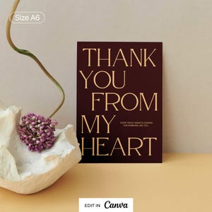 Puede incluir: Una tarjeta rectangular A6 con fondo granate oscuro y letras doradas con serifa que dicen THANK YOU FROM MY HEART y EVERY PIECE I MAKE IS LOOKING FOR SOMEONE LIKE YOU. La tarjeta está colocada junto a una concha blanca texturizada.