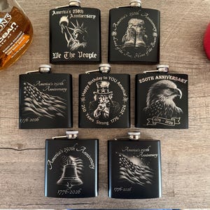 May include: A collection of black flasks with silver tops, each engraved with patriotic designs and the text "America's 250th Anniversary" and "1776-2026". Designs include the Statue of Liberty, an American flag, and an eagle.