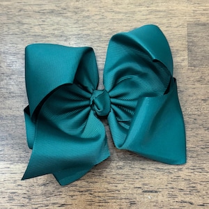 May include: A dark teal hair bow constructed from ribbed grosgrain ribbon. The bow features a central knot with two large, symmetrical loops on each side, creating a voluminous, multi-layered appearance with a distinct horizontal texture.