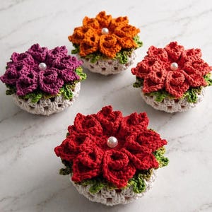 Pode incluir: Quatro bases de flores de crochê feitas à mão em tons de vermelho, laranja, roxo e coral. Cada base apresenta um centro de pérola e acabamento verde e branco. As bases têm aproximadamente 10 cm de diâmetro.