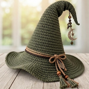 May include: A pointed olive green crochet hat featuring a wide brim and a textured knit pattern. The hat is adorned with a brown braided band, a bow, and dangling charms including wooden beads, metal leaves, and a crescent moon with a star.