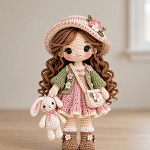 Pode incluir: Uma boneca de crochê feita à mão com longos cabelos castanhos ondulados, vestindo um vestido rosa, um cardigã verde com pequenas flores, um chapéu combinando e botas marrons. A boneca carrega uma pequena bolsa transversal creme e um coelho de crochê.