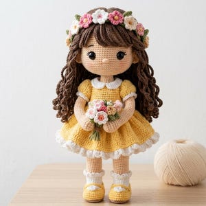 Pode incluir: Uma boneca de crochê feita à mão com longos cabelos castanhos cacheados, vestindo um vestido amarelo com gola e acabamento brancos. A boneca usa uma coroa de flores, segura um pequeno buquê de flores de crochê e usa meias brancas com sapatos amarelos.