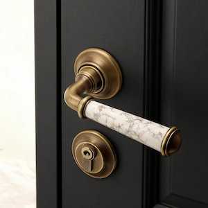 May include: Close-up of a door handle set with a brass finish and a white marble-patterned handle. The set includes a round backplate, a curved lever, and a keyhole. The door is painted black.