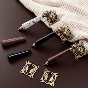 May include: Three decorative door handles with brass hardware and different handle materials: white marble, black, and dark wood. Two additional handle pieces and two keyhole covers are also present.