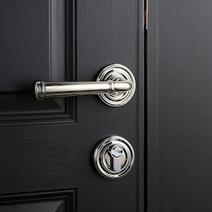 May include: Polished silver door handle and keyhole on a black door. The lever handle has a cylindrical grip and decorative backplate. The keyhole is circular. The door is painted black.