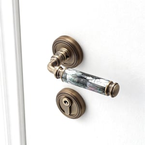 Könnte beinhalten: Antike Türgriffgarnitur aus Messing mit dekorativem, irisierendem Griff. Der Griff und die Schlüssellochplatte sind an einer weißen Tür montiert. Das Design des Griffs weist ein Mosaik aus Farben auf.