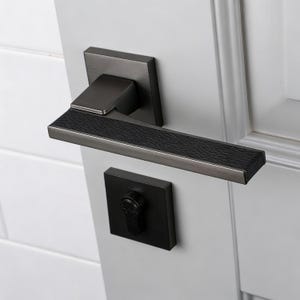 Peut inclure: Ensemble de poignée de porte moderne de couleur gris foncé, avec une plaque arrière carrée et une poignée texturée. L'ensemble comprend une serrure à pêne dormant carrée assortie, le tout monté sur une porte blanche.