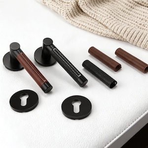 Peut inclure: Ensemble de poignées de porte noires avec des accents de cuir. Une poignée a du cuir marron, une autre du cuir noir avec des coutures blanches. Comprend des rosaces assorties et des manchons en cuir.