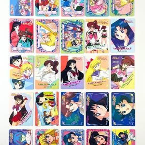 以下が含まれることがあります： カラフルなセーラームーンのトレーディングカードのコレクション。各カードには、鮮やかな色の異なるキャラクターが描かれており、日本語のテキストと装飾的なボーダーが付いています。カードは長方形で、カードストックで作られているようです。