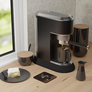 May include: A black and silver espresso machine with a mug of coffee. A black plate with a slice of cake, a coaster with a coffee design, and a small pitcher are on a wooden surface. A sugar bowl and a canister are also present.