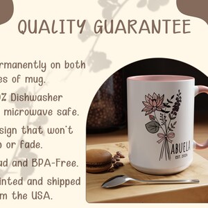 May include: White ceramic mug with a pink interior and handle. The mug features a floral bouquet design with the word "ABUELA" and "EST. 2000". The mug is on a wooden surface with a spoon and a macaron.