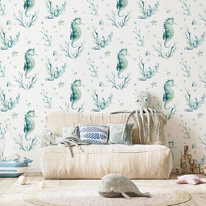 May include: A room with a white seahorse and coral wallpaper. A beige sofa is in front of the wall, with decorative pillows and stuffed animals. A toy sailboat, wooden blocks, and a whale-shaped stuffed animal are on the floor.