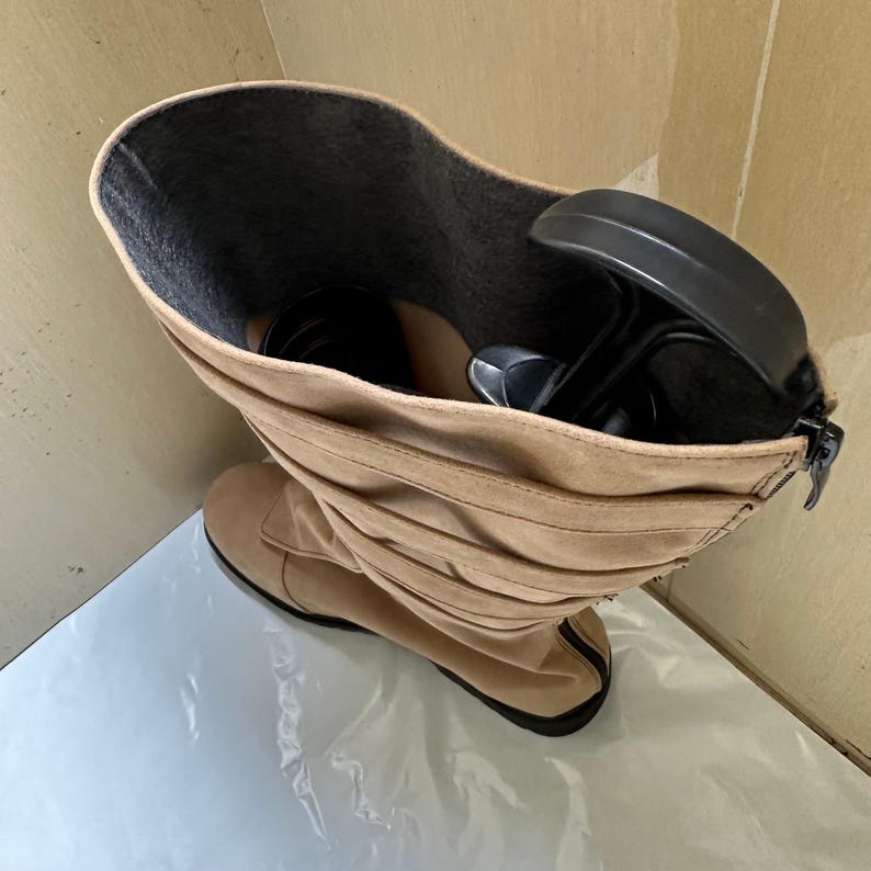 May include: Tan suede knee-high boot with a black sole and a zipper closure. The boot has a ruched design and a dark gray interior. A black shoe tree is inside the boot.