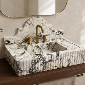May include: A rectangular marble sink featuring a white base with prominent dark purple and grey veining. The sink has a fluted exterior texture and an arched backsplash. It is equipped with a brass faucet and two matching brass handles.