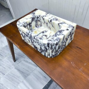 May include: A rectangular stone sink featuring a white base with prominent dark purple and black veining. The exterior of the basin is constructed with a series of vertical fluted columns, creating a textured, ribbed appearance around the entire perimeter.