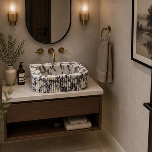 May include: A rectangular bathroom sink featuring a white and dark blue marbled pattern with a fluted exterior texture. The sink is mounted on a wooden vanity cabinet with a light stone countertop, brass faucet, and matching brass wall-mounted lighting.