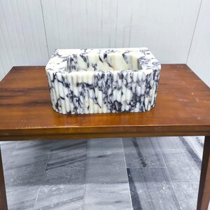 May include: A rectangular sink basin featuring a white and dark purple marbled pattern with a fluted, vertically ribbed exterior texture. The basin has a deep, open interior and a smooth, polished finish throughout its entire outer surface.