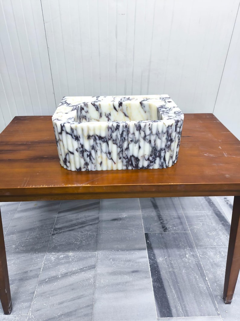 May include: A rectangular sink basin featuring a white and dark purple marbled pattern with a fluted, vertically ribbed exterior texture. The basin has a deep, open interior and a smooth, polished finish throughout its entire outer surface.