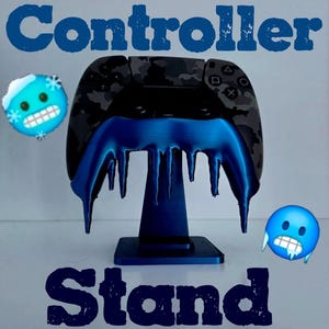 Puede incluir: Un mando negro y gris camuflaje apoyado en un soporte azul. El soporte tiene un diseño azul goteante, con la palabra "Controller" arriba y "Stand" abajo en texto azul. Dos emoji azules con cristales de hielo a cada lado.