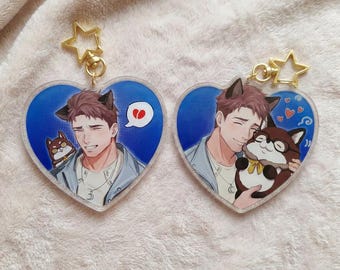 May include: Two heart-shaped acrylic keychains with gold star-shaped clasps. Each features an illustrated character with animal ears. The left keychain shows a character with a broken heart speech bubble. The right shows a character holding a plush toy.
