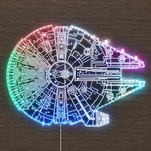 Könnte beinhalten: Eine LED-Wandleuchte in Form des Millennium Falcon Raumschiffs. Das Design zeigt filigrane weiße Linien, die die mechanische Struktur des Schiffes darstellen und von einem leuchtenden Farbverlauf in Rot, Grün und Blau erhellt werden.