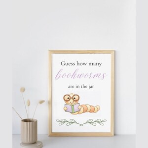 Op de afbeelding: Een ingelijste print met de tekst "Raad hoeveel boekenwormen er in de pot zitten". De print toont een stripboekworm met een bril en een boek. De print zit in een houten lijst.